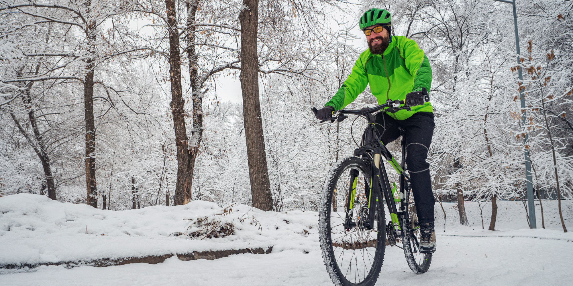 Mann fährt mit einem Fahrrad durch eine Schneebedeckte Gegend mit in Winterbekleidung.