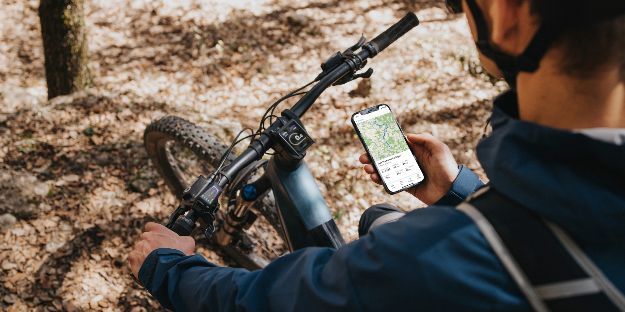 Mann sitzt auf einem e-Mountainbike und schaut auf sein Handy indem die e-bike-Flow App geöffnet ist