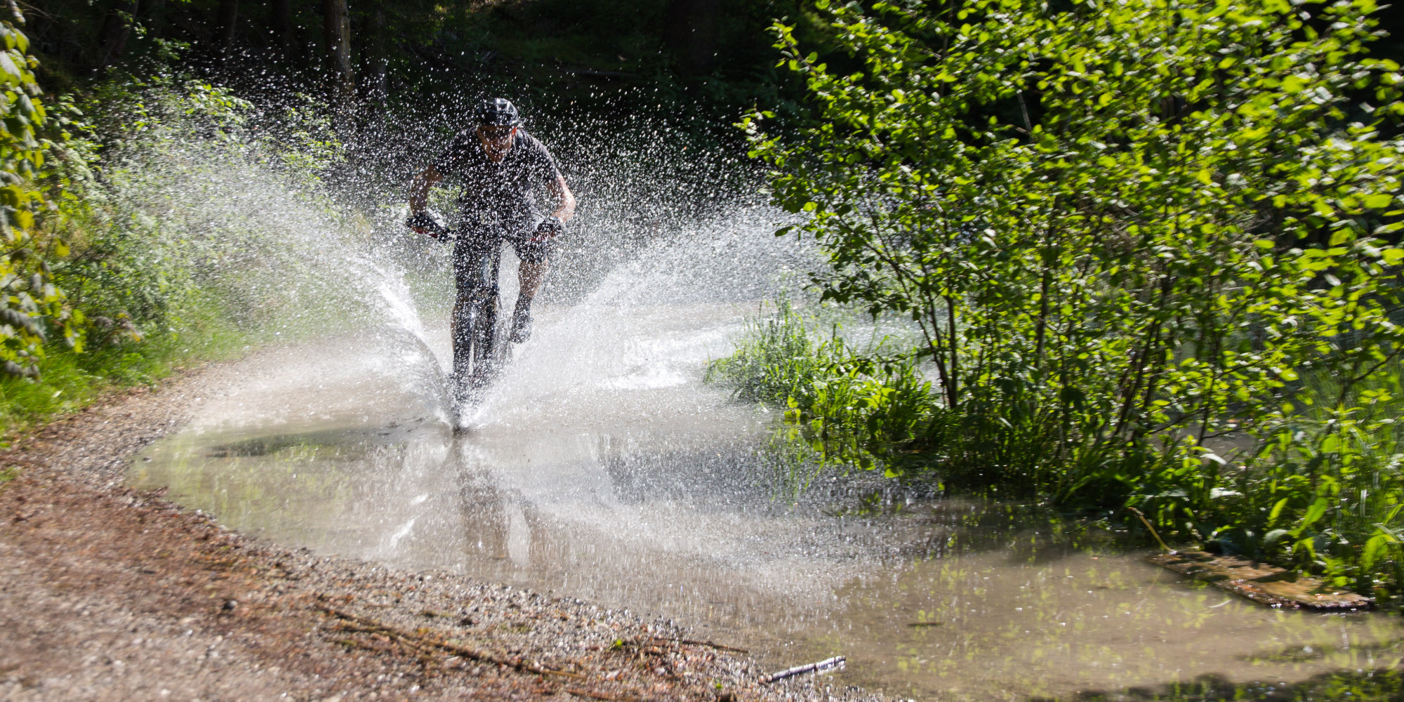 Radler fährt mit einem E-Mountainbike durch eine Pfütze