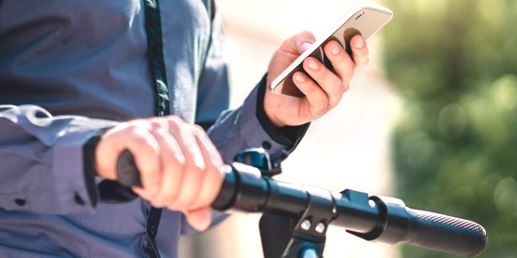 Person mit Smartphone in der Hand steht auf einem E-Scooter