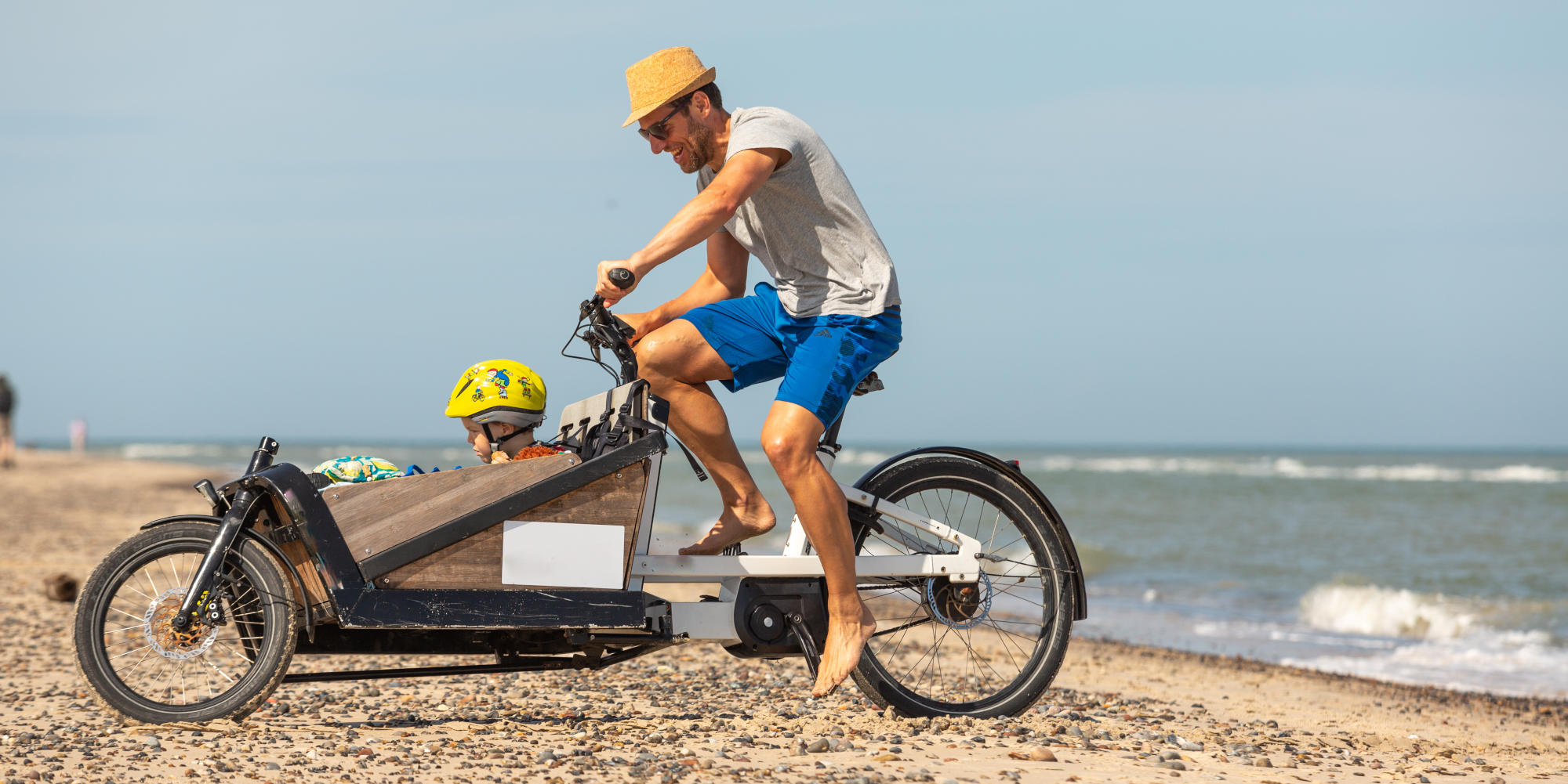 Mann mit Kind und Lastenrad am Strand.