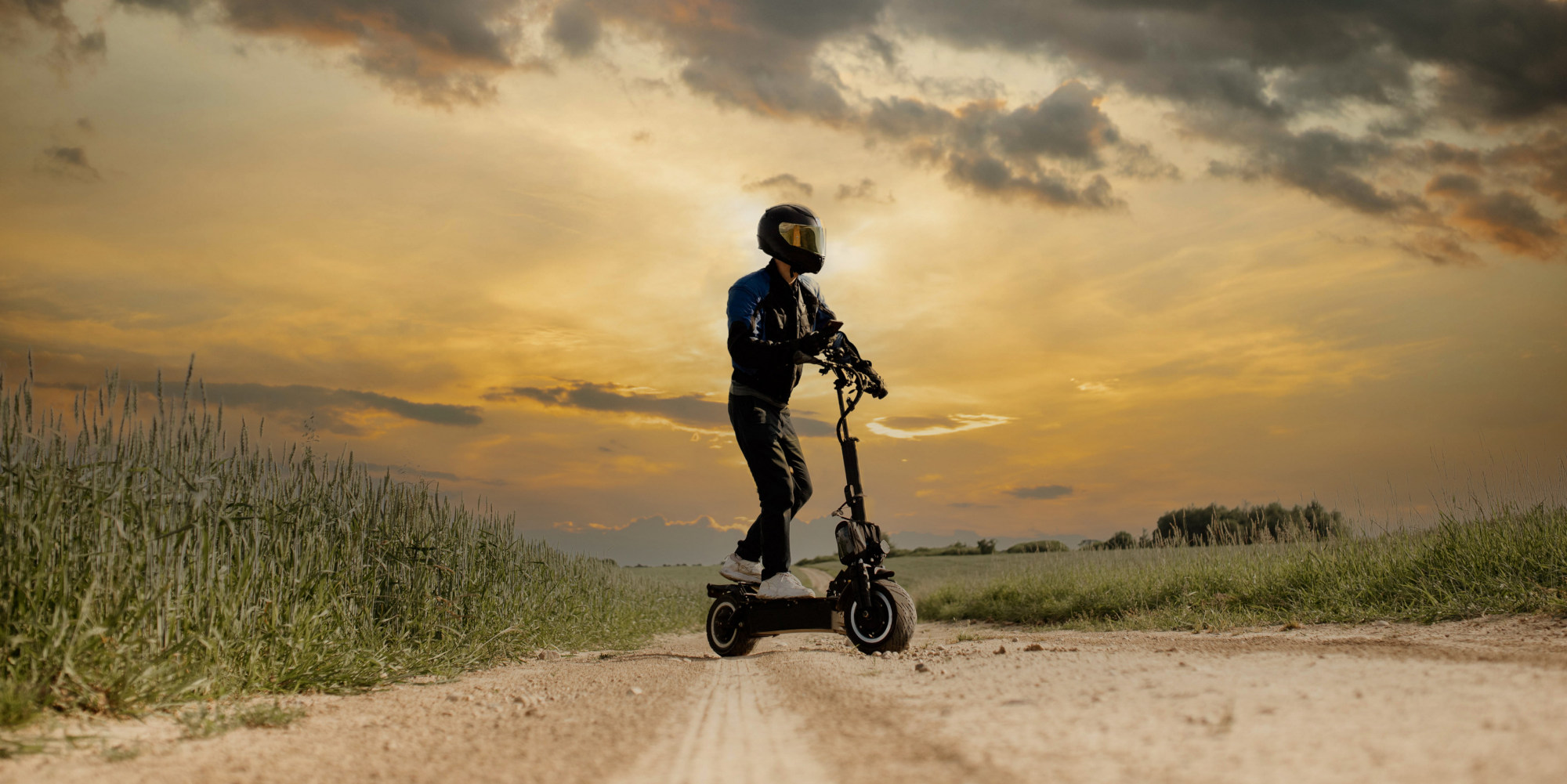 Mann mit Helm steht auf E-Scooter neben einem Feld.