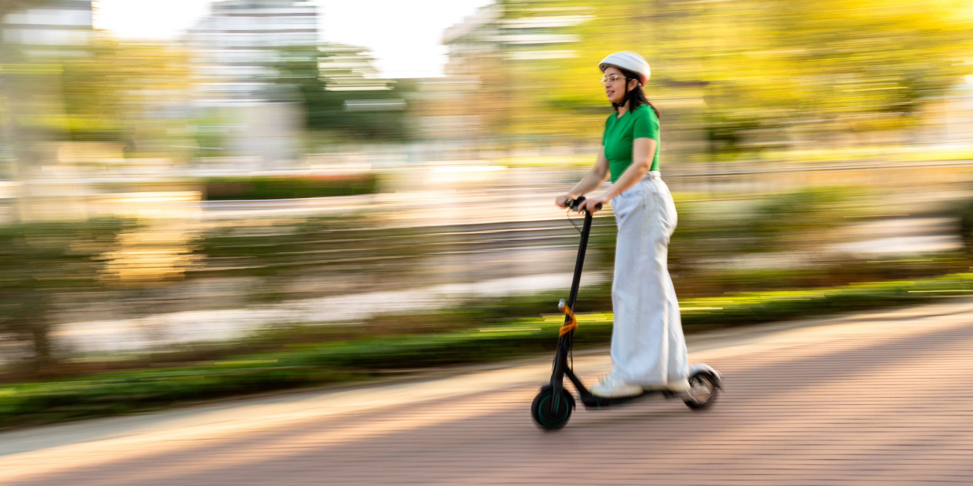 Frau mit Helm fährt mit E-Scooter über einen Weg.