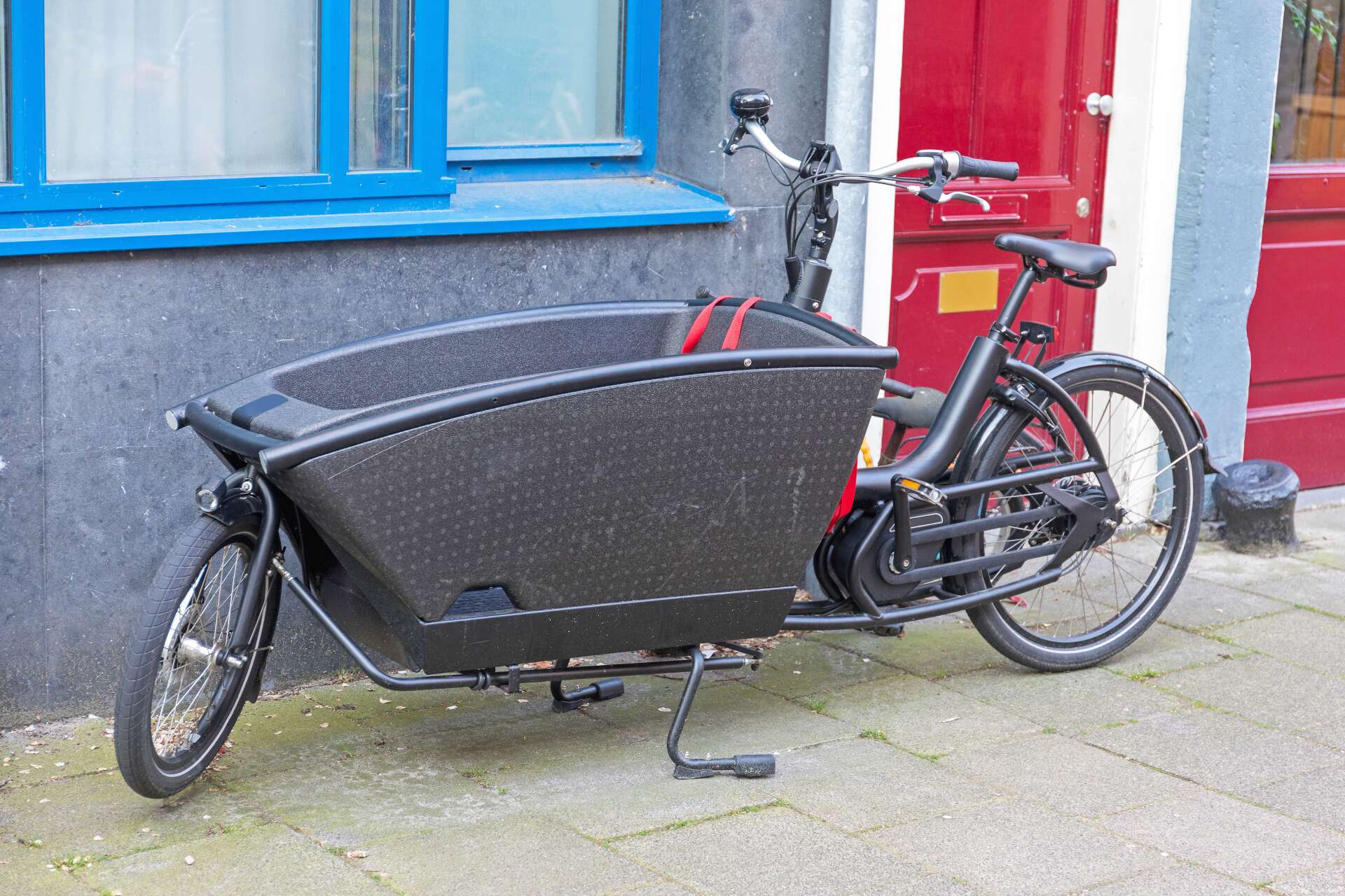 Schwarzes Lastenrad mit großer Transportbox im vorderen Teil steht vor einer Hauswand.