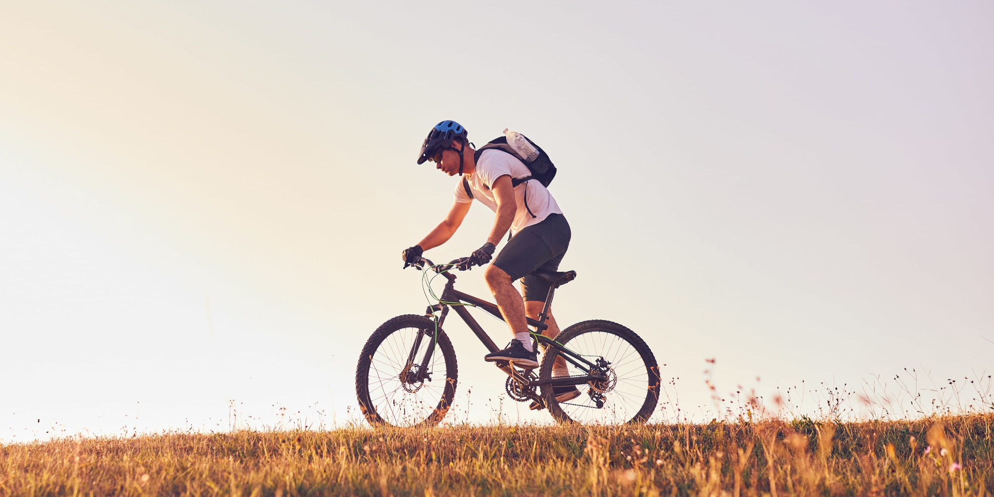 Mann mit Helm, fährt mit E-MTB über Wiese