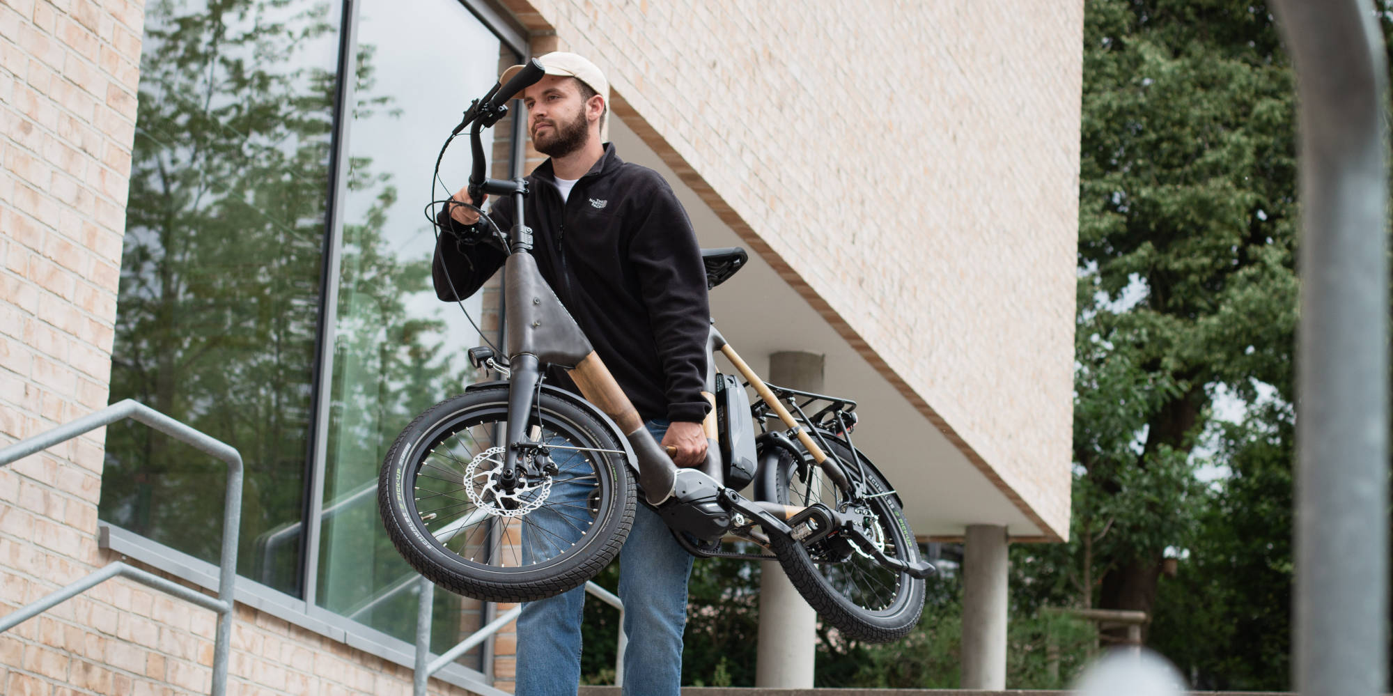 Mann trägt Bambus E-Bike die Treppe hinunter.