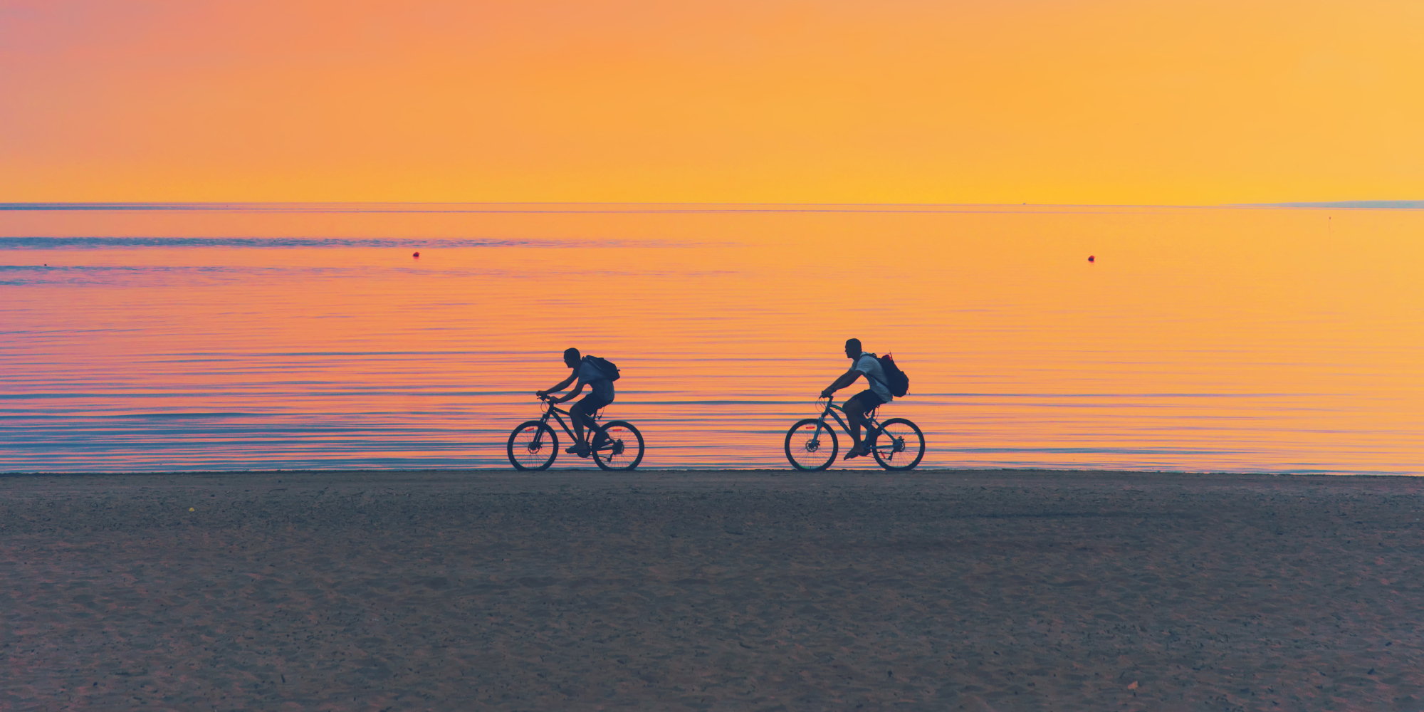 Zwei Radfahrer fahren am Strand vor dem Sonnenuntergang