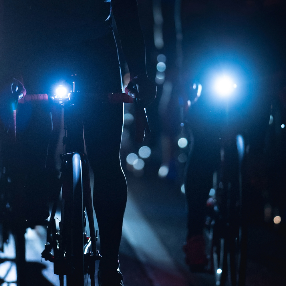 Eine Gruppe Fahrradfahrer fährt bei Nacht Fahrrad in der Stadt und haben Lichter an.