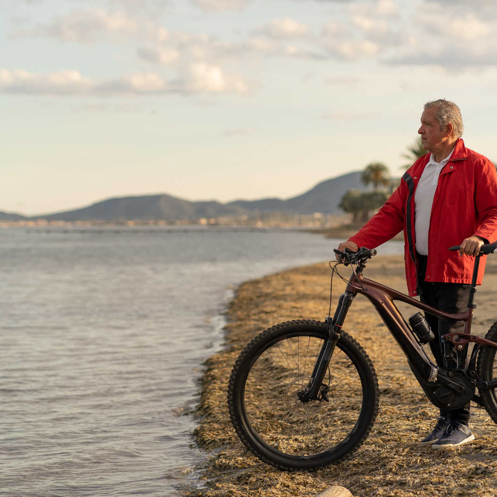 Mann steht mit Mountainnbike am Strand