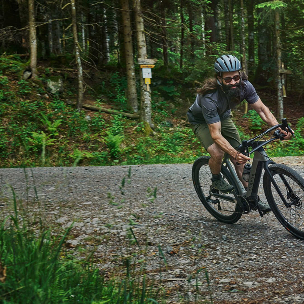 Mann fährt auf Canyon E-Gravel durch Wald.