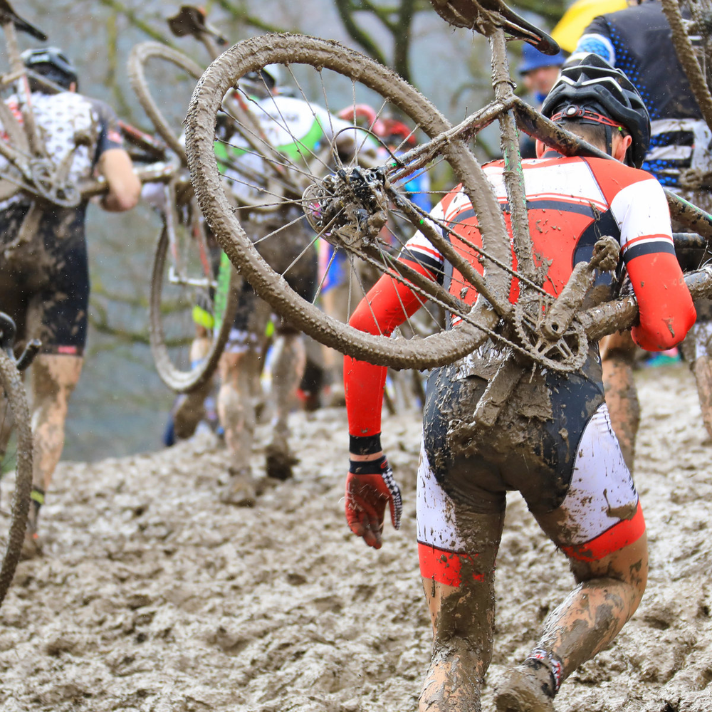 Radsportler laufen durch Schlamm mit ihren Fahrrädern