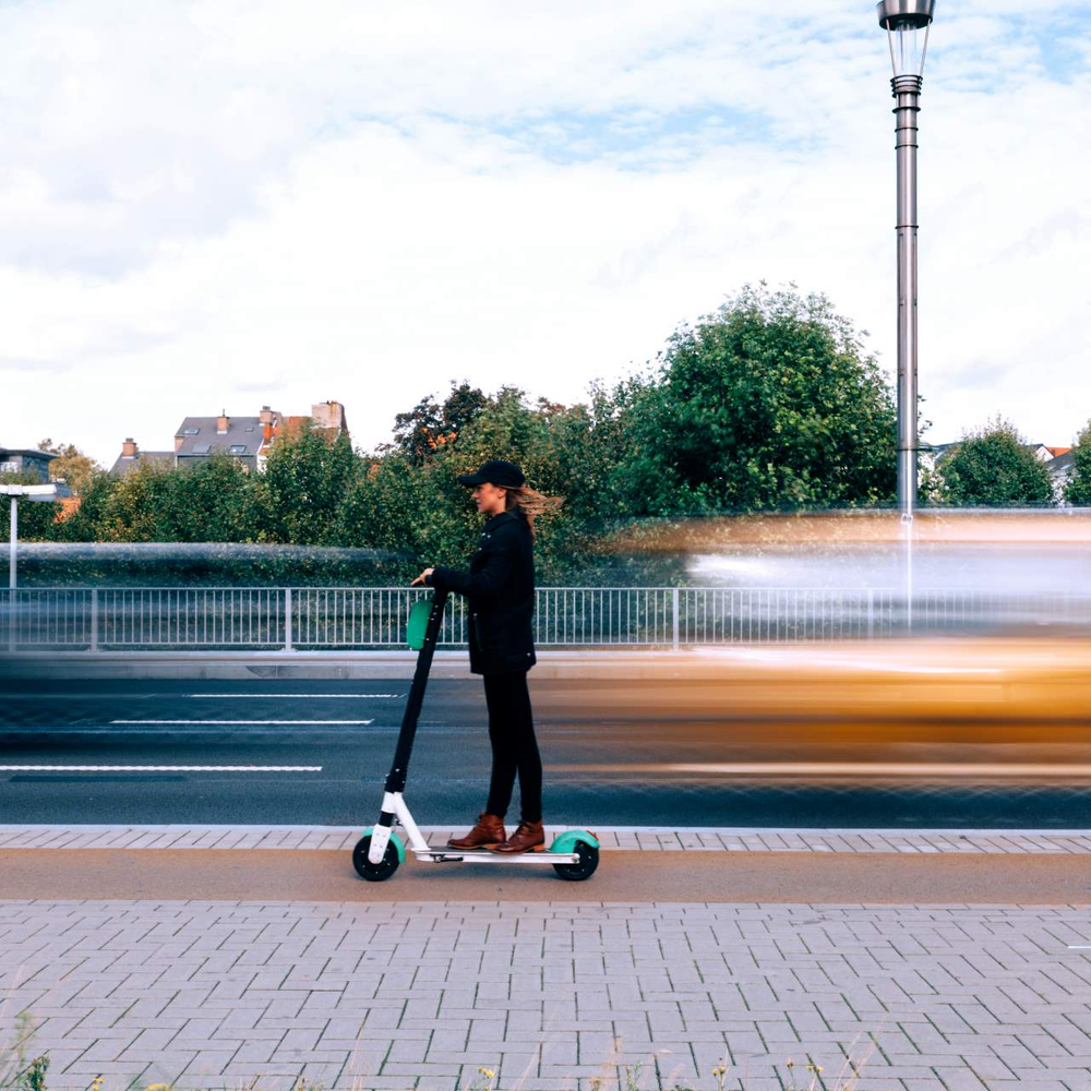 Frau auf E-Scooter fährt an viel befahrender Straße