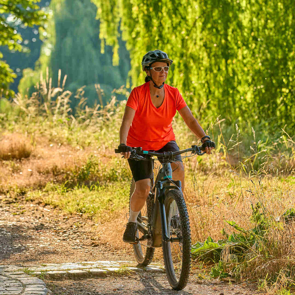 Frau fährt auf E-Crossbike über Natur-Radweg.