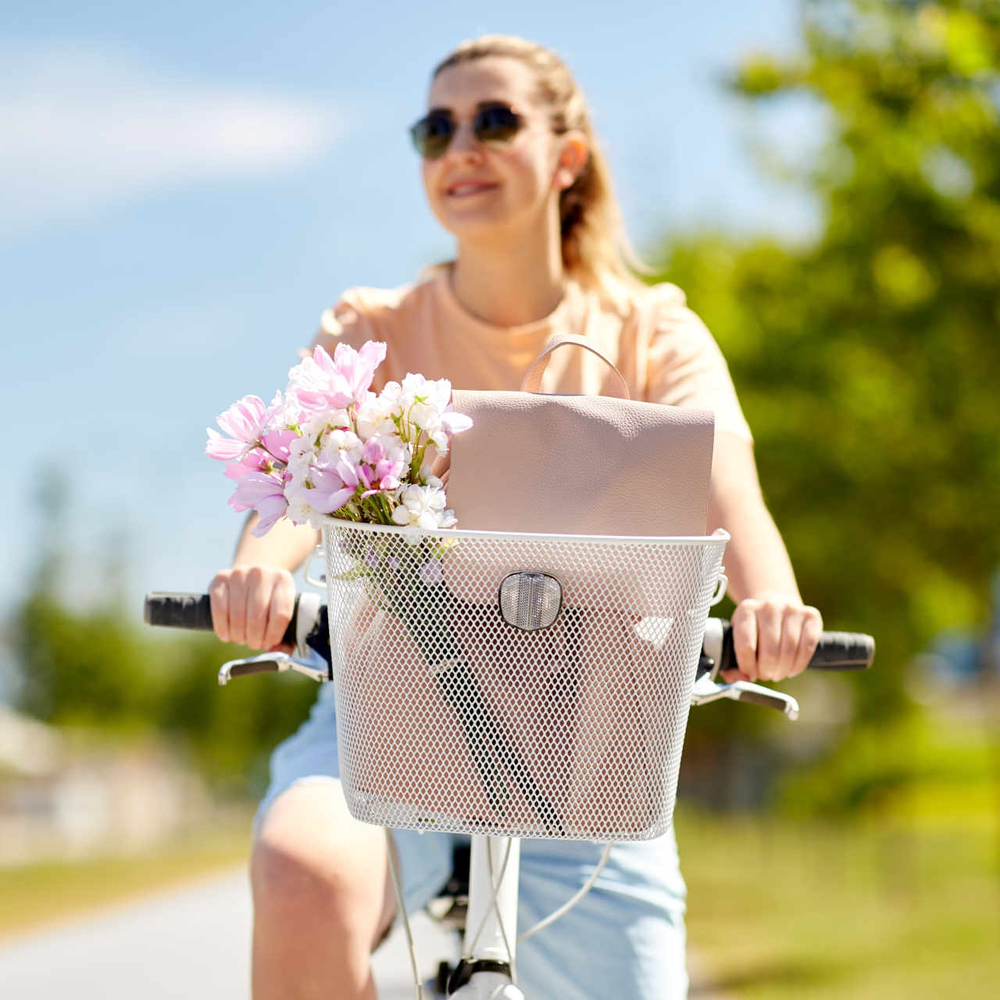 Frau fährt auf Rad mit Fahrradkorb durch eine sonnige Landschaft