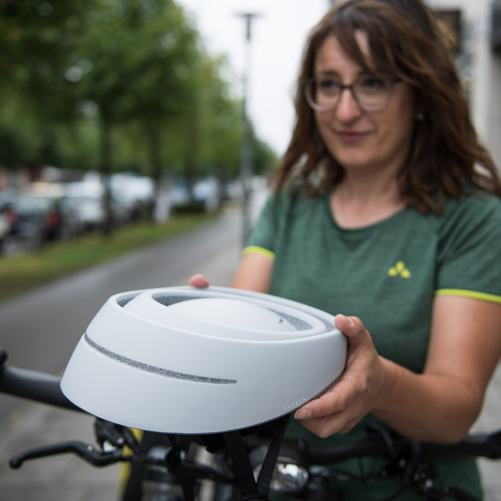 Radfahrerin hält zusammengefalteten Helm von Closca in der Hand.