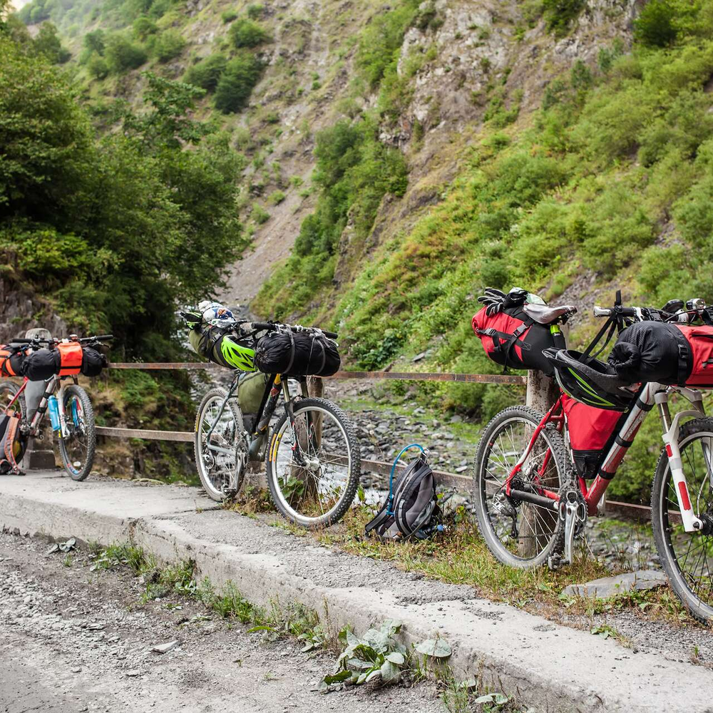 Drei Fahrräder in bergigem Gelände, die mit rot-schwarzen Bikepacking-Taschen versehen sind