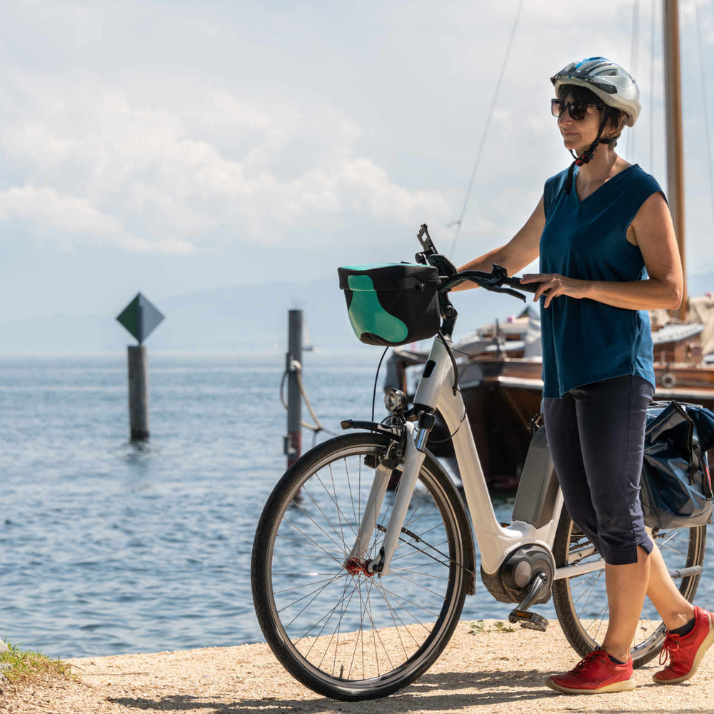 Frau mit Helm steht neben Fahrrad an einem See.