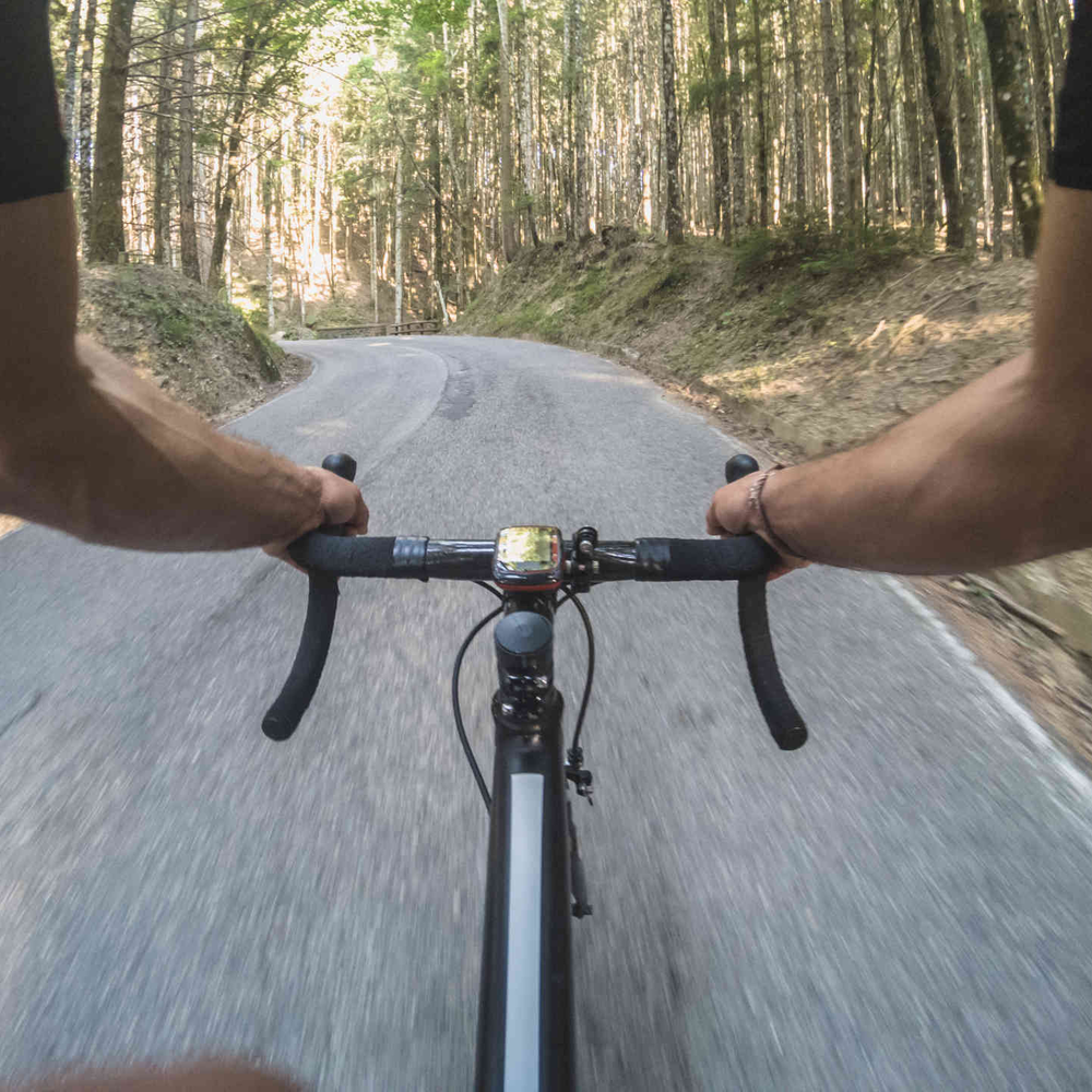 Mann auf Rennrad fährt auf Straße durch Wald.