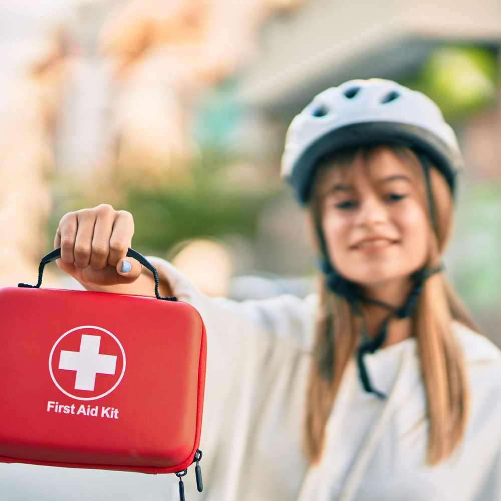 Frau hält eine Reiseapotheke in der Hand und trägt einen Fahrradhelm