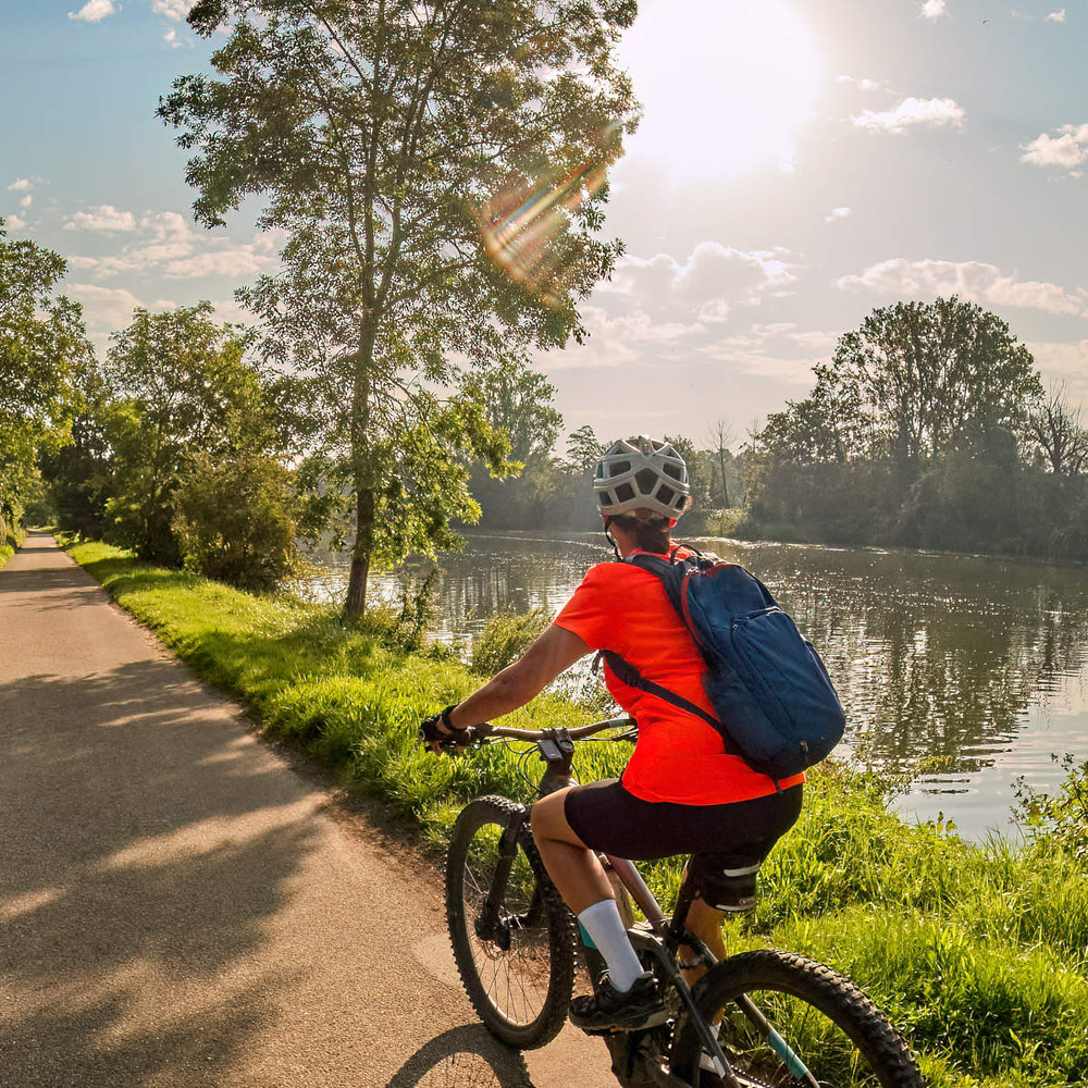 Frau fährt an einem Flussufer mit einem E-Bike entlang