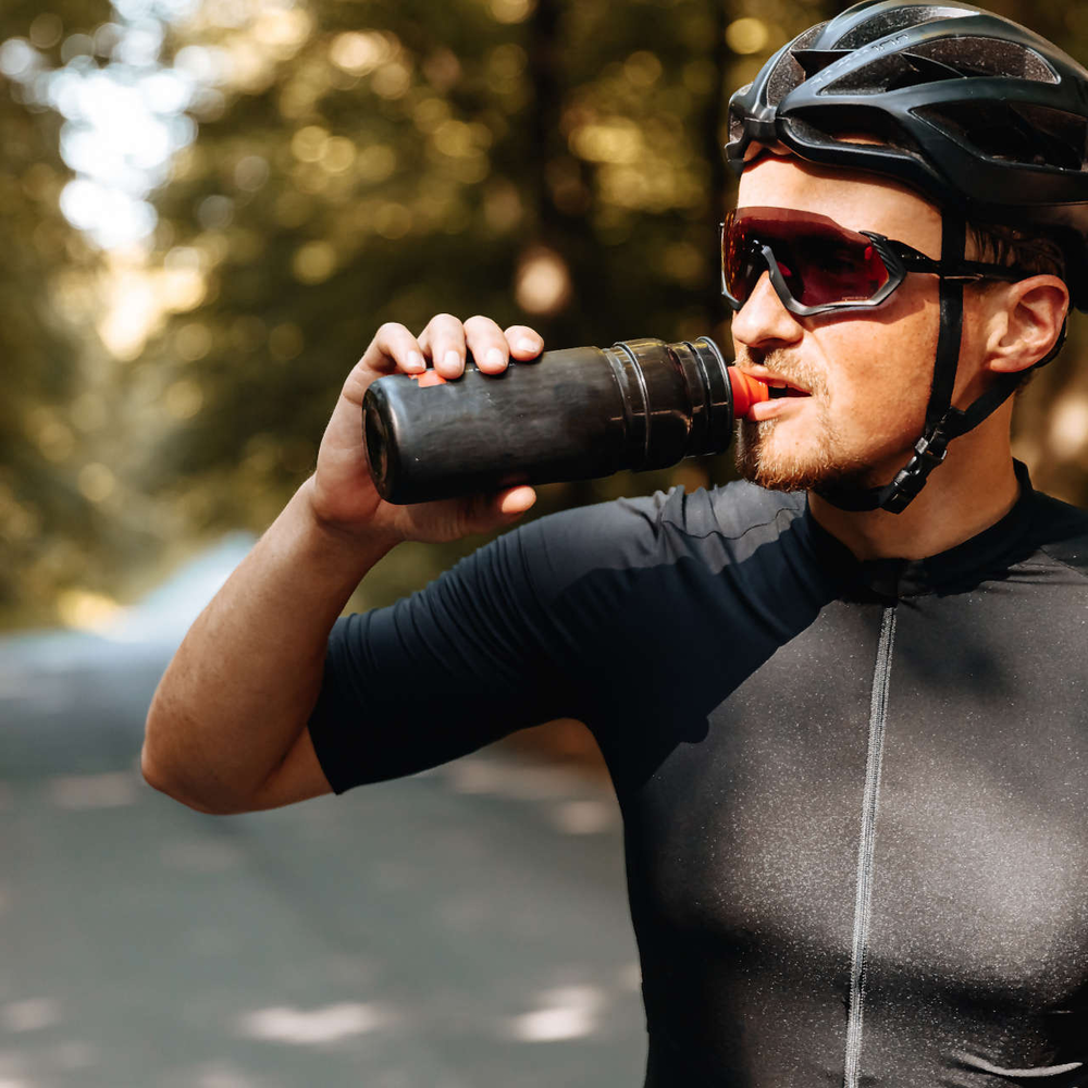 Radfahrer mit Sonnenbrille trinkt aus Trinkflasche