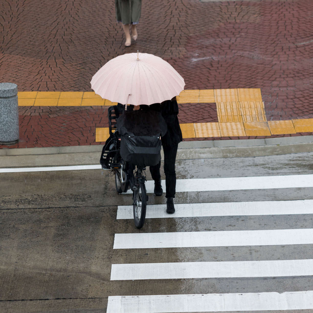 Person schiebt Fahrrad bei Regen über einen Zebrastreifen