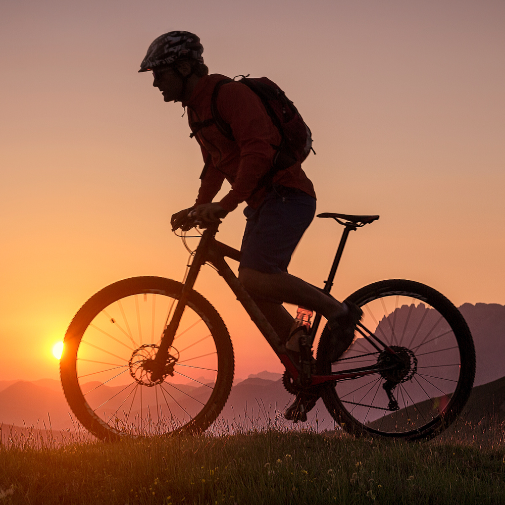 Mann fährt mit einem Mountainbike durch Gebirge im Sonnenuntergang